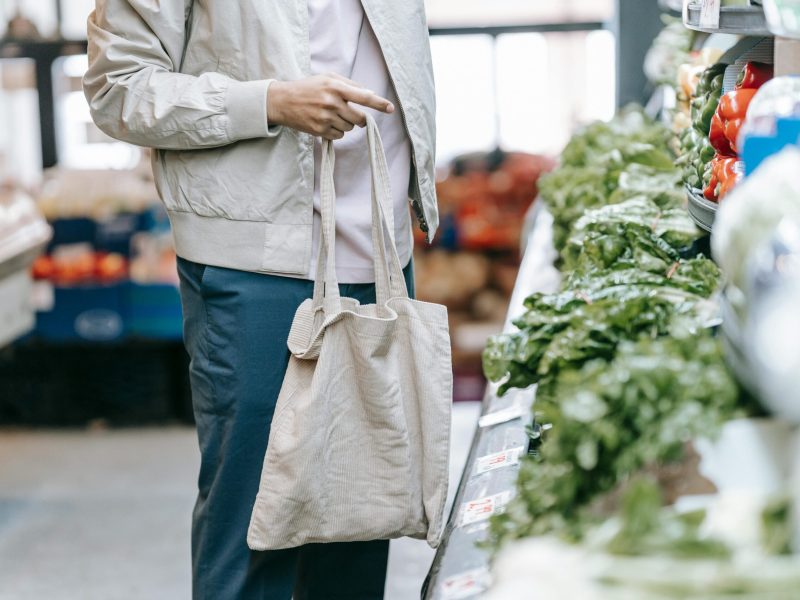 Man selecting fresh vegetables in a grocery store with an eco-friendly bag.